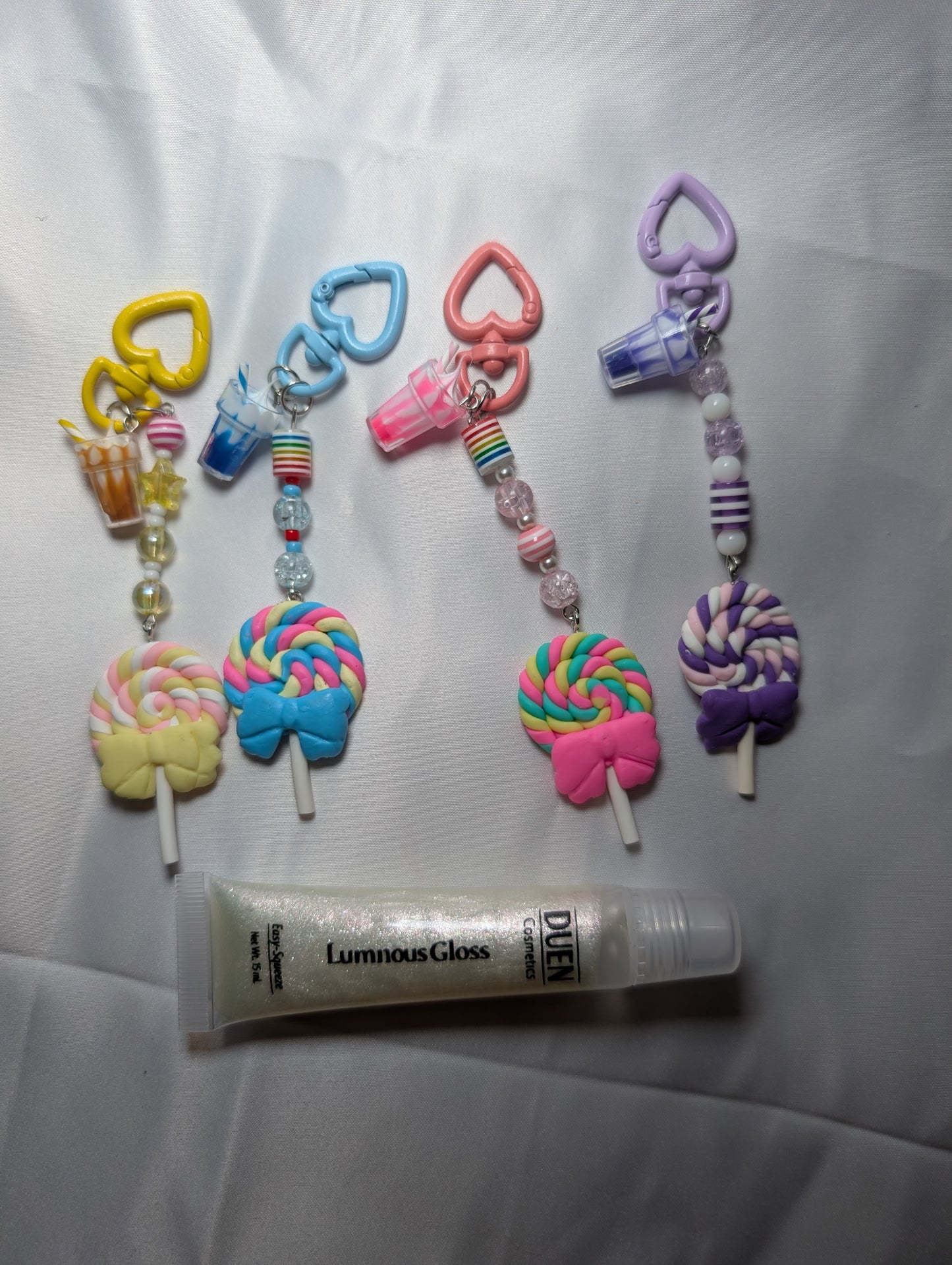Colorful keychains shaped like lollipops and a tube of Luminous Gloss on a white background