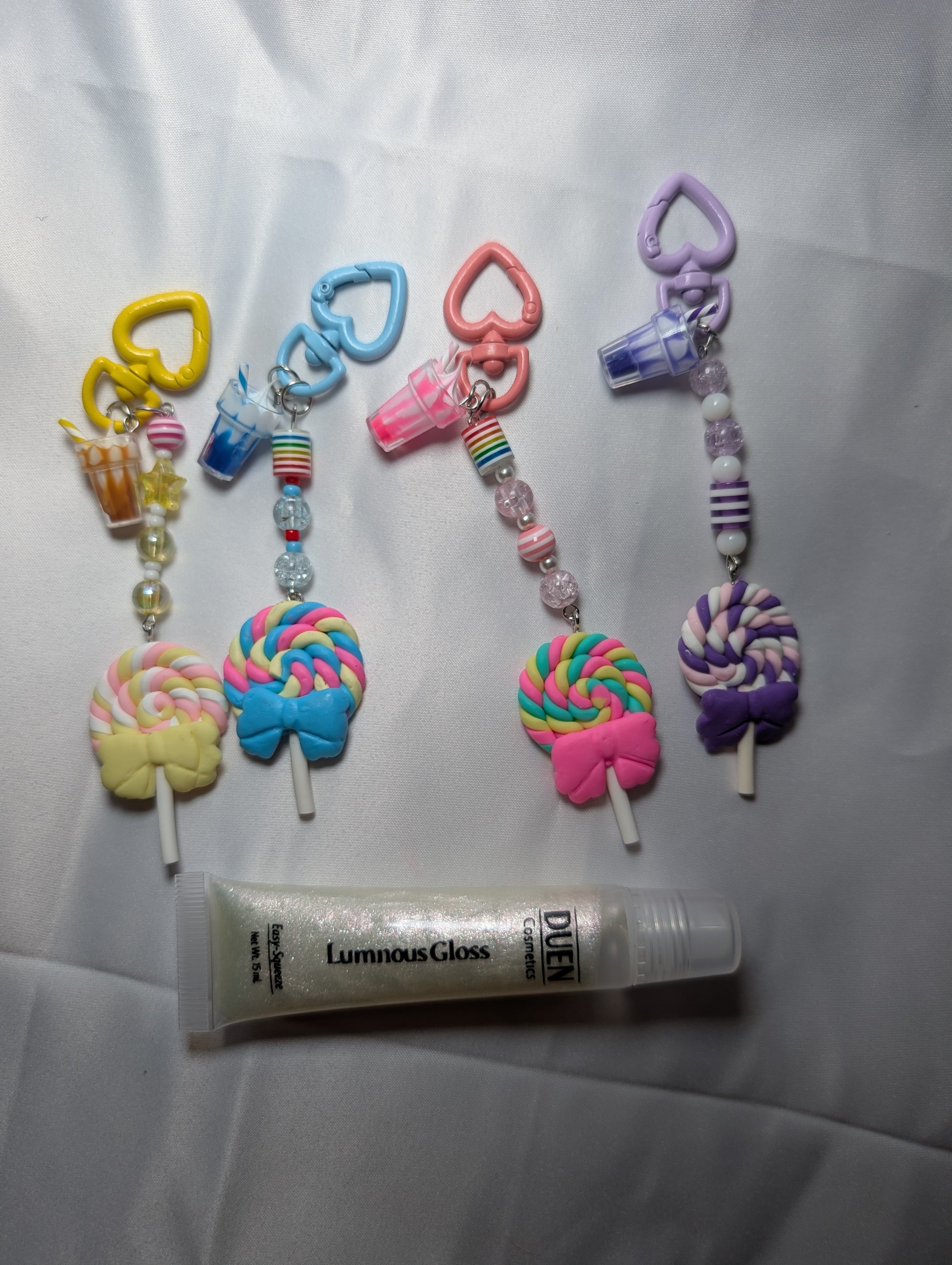 Colorful keychains shaped like lollipops and a tube of Luminous Gloss on a white background