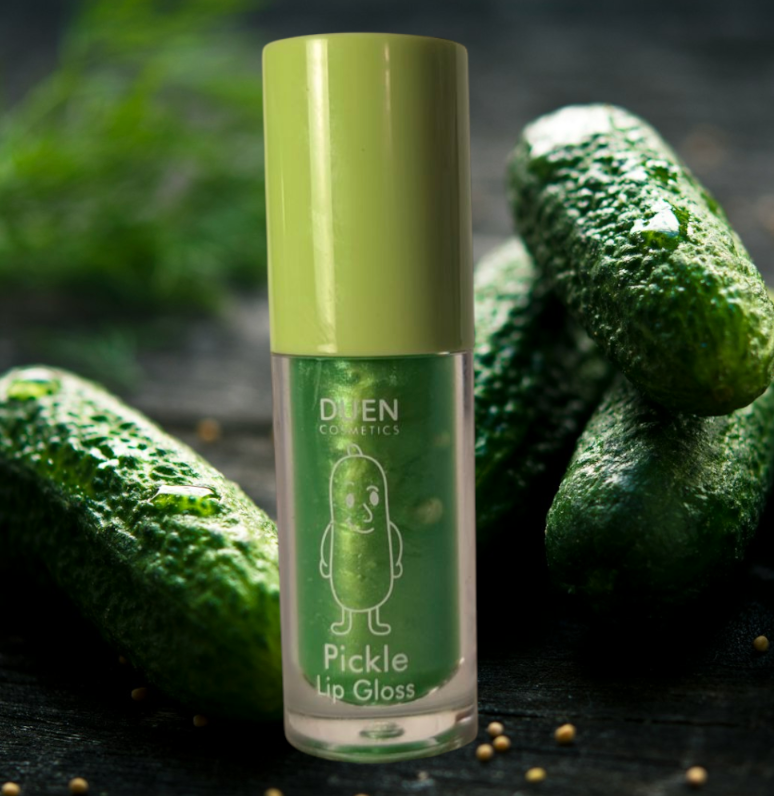 Pickle Lip Gloss tube with green cap, smiling pickle character, and four dill pickles in the background