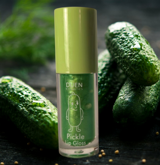 Pickle Lip Gloss tube with green cap, smiling pickle character, and four dill pickles in the background